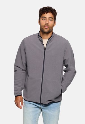 Chaqueta gris con cremallera y cuello alto, con tejido texturizado, bolsillos laterales y cremallera oscura en contraste. Ajuste casual, diseño sencillo.