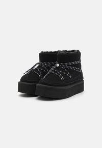 Botines negros con una suela de plataforma gruesa, hechos de ante, con cordones de patrón en blanco y negro y un interior suave y peludo.