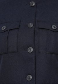 Marinekék gombos ing, amely két mellzsebből, fekete műanyag gombokból és puha, strukturált anyagból készült. Tailored, strukturált dizájn.