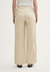 Pantalons larges beiges avec une texture lisse et un subtil motif de rayures; dotés de deux poches arrière et d'une taille haute.
