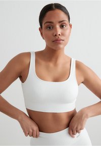 Hvit ribbestrikket crop top med brede stropper og firkantet utringning, med en tettsittende design og subtilt teksturert mønster.