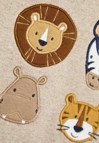 Zacht beige stof met geborduurde dierenontwerpen: een leeuw, nijlpaard en tijger, met gebruik van bruine, gele, zwarte en witte garens.