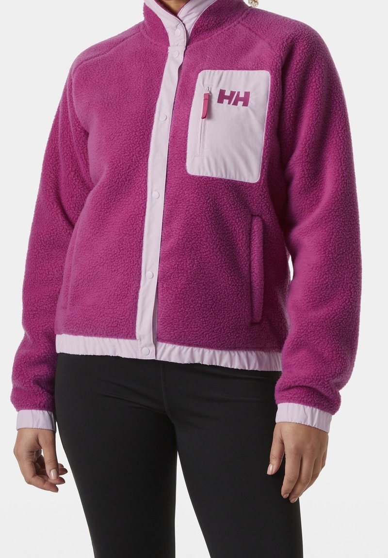 Chaqueta de forro polar morada con un bolsillo con cremallera rosa, cierre de botones y cintura elástica. Presenta una textura suave y puños de manga en contraste.