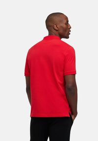 Polo shirt rossa con colletto classico, maniche corte e dettagli con spacco laterale, realizzata in tessuto morbido, mostrata da una vista laterale.