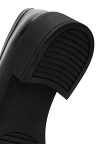 Zwarte sandaal met een brede, gladde bovenkant, een gestructureerde, geribbelde zool en een gebogen hak met horizontale groeven voor grip.