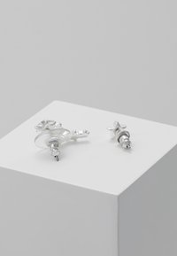 Sølvøreringe med et cirkulært design og en lille stjerneaccent, poleret finish og nålelukning.