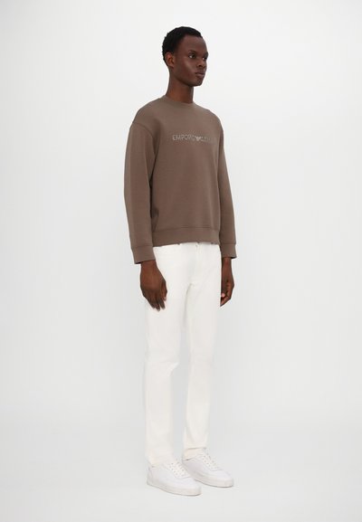 Brown sweatshirt with ribbed cuffs and neckline, featuring "EMPORIO ARMANI" logo. Paired with slim-fit white jeans and white sneakers.