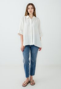 Oversized white linen shirt with a button-up front and roll-up sleeves, paired with faded blue denim jeans and brown flip-flops.