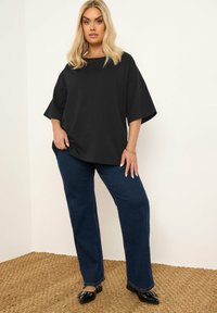 Svart oversized t-shirt med bred halsringning och korta ärmar, kombinerad med mörkblå raka jeans och svarta platta skor.