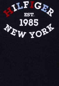T-shirt blu con scritte bianche e colorate: "HILFIGER EST. 1985 NEW YORK." Tessuto semplice e morbido con un classico design a girocollo.
