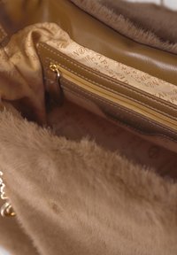 Interno di una borsa in finta pelliccia marrone con fodera in tessuto beige, tasca in pelle con zip dorata e una parte della tracolla in catena dorata visibile.