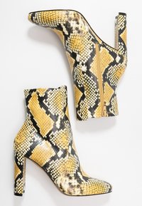 Bottines à chevilles imprimées python en jaune, noir et blanc. Dotées d'un talon stiletto et d'une fermeture éclair latérale. Surface texturée sur toute la chaussure.