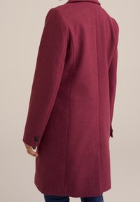 Cappotto in lana color bordeaux con colletto a revers, maniche lunghe e polsini con bottoni; texture liscia con design posteriore dritto e dettagli cuciti.
