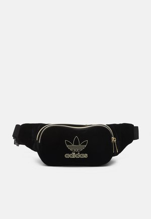Czarna nerka Adidas ze złotym zamkiem błyskawicznym i logo, regulowanym paskiem oraz główną kieszenią na zamek na białym tle.