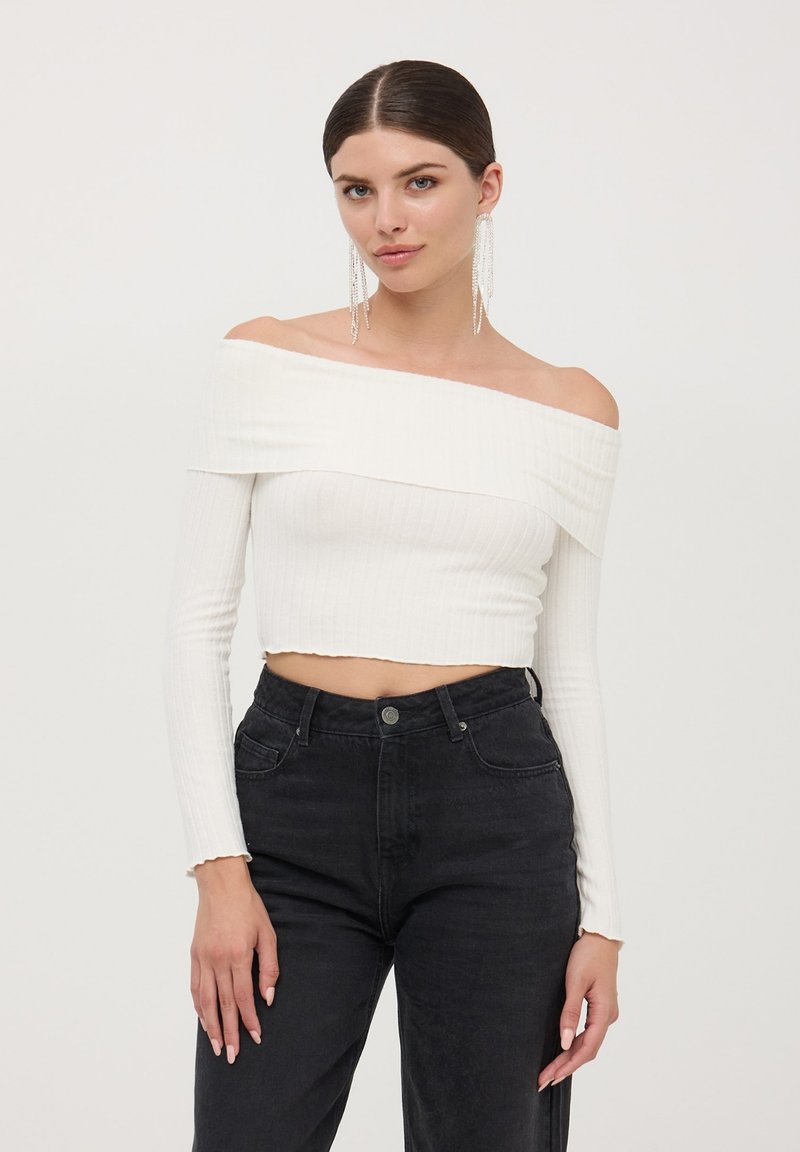 Top a maniche lunghe aderenti bianco a coste, scoperto sulle spalle, abbinato a jeans in denim neri a vita alta.