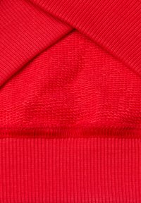 Tessuto a maglia rossa con una superficie testurizzata, caratterizzato da bordi a coste lisci e schemi di tessitura variabili per profondità e dimensione.