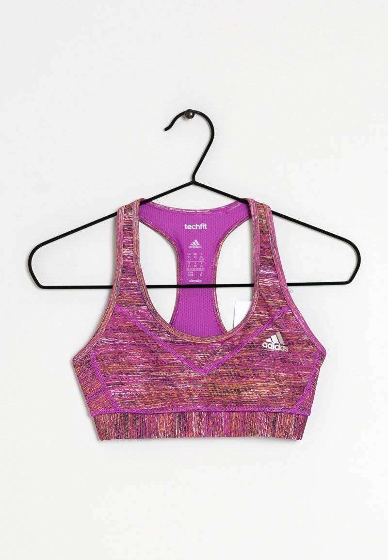 Brassière de sport Adidas techfit violette et rose à motifs suspendue à un cintre noir sur fond blanc.