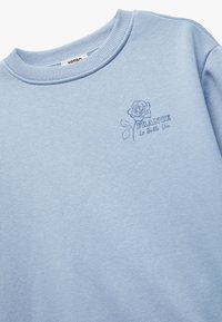 Lichtblauwe sweatshirts met een geribbelde ronde hals. Kenmerkt een geborduurd rozenafbeelding en de tekst "FRANKRIJK La Belle Vie" in het blauw.