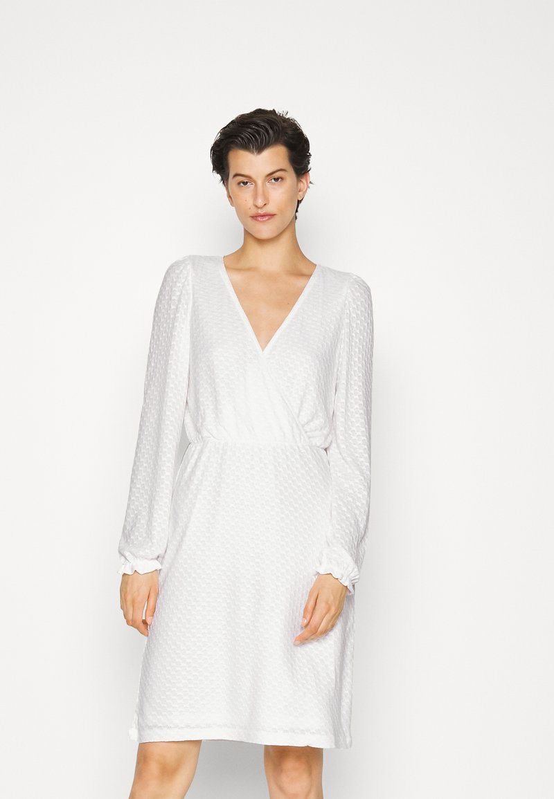 Vestido branco com decote em V, mangas bufantes longas e tecido texturizado. Apresenta uma cintura elástica e punhos franzidos para um ajuste confortável.