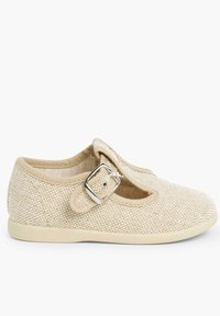 Zapato Mary Jane de tela beige con diseño de malla, punta redonda, correa ajustable y detalle de hebilla plateada. Suela suave y flexible para mayor comodidad.