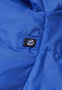 Tissu rembourré bleu à texture lisse, doté d'une fermeture à bouton-pression noire et de coutures apparentes. Le matériau semble léger et brillant.