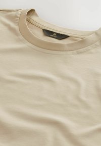Beige bomulds t-shirt med rund halsudskæring og blød tekstur, med mærkets label synlig på den indre hals.