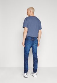 Camiseta de algodón azul con mangas cortas, combinada con jeans de denim oscuros de corte ajustado. Zapatillas deportivas blancas casuales completan el atuendo.