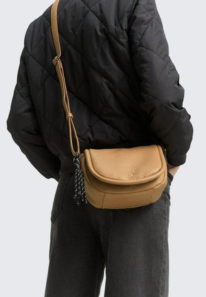 Braune Leder-Crossbody-Tasche mit einer strukturierten Oberfläche und einem gebogenen Deckel, ausgestattet mit einem langen Riemen, der mit einem schwarz-weißen Quastenakzent verziert ist.