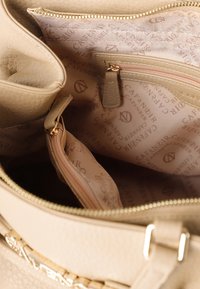 Beige textuur handtas interieur met meerdere ritssluitingen, gevoerd met een stof met logo-patroon. Hardware in goudtint.