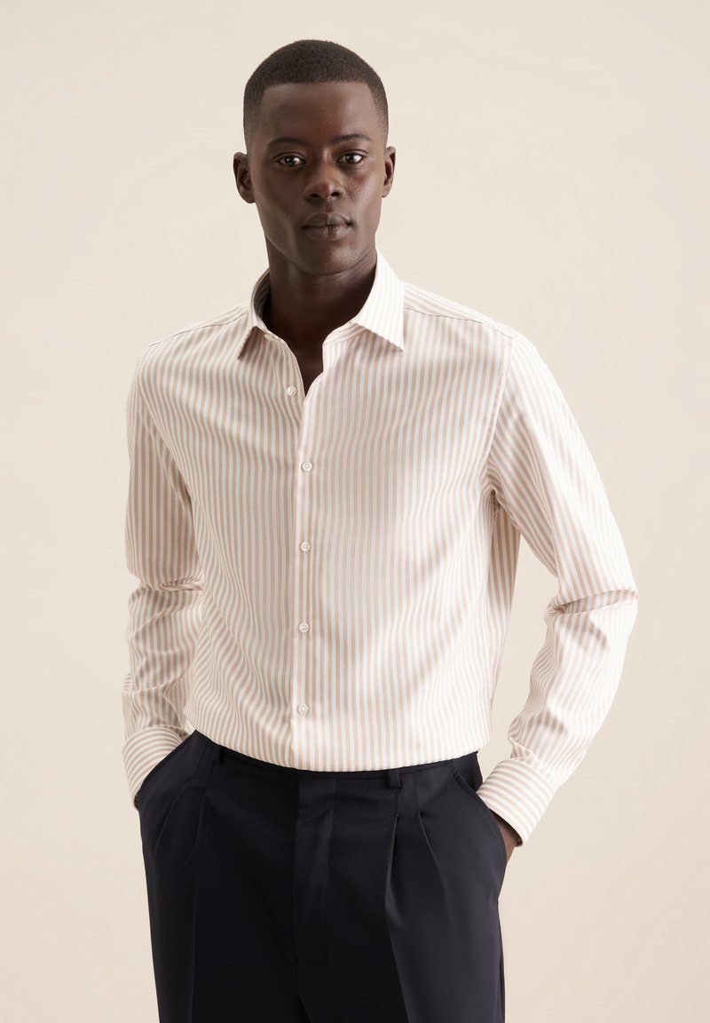 Camicia da uomo a righe rosa chiaro e bianche, con colletto a punte, maniche lunghe, chiusura con bottoni e tessuto strutturato. Indossata con pantaloni scuri.