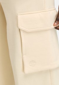 Beige katoenen joggers met een grote zijzak en een subtiele boomlogo geborduurd aan de basis van de zak. Soepele textuur, ontspannen fit.