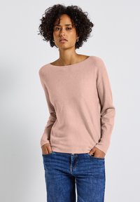 Helle rosa gestrickte Sweatshirt mit weitem Bootsausschnitt und gerippten Ärmelbündchen, kombiniert mit blauen Denim-Jeans. Weiche Textur, entspannter Schnitt.