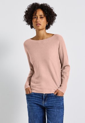Pull en tricot rose clair avec un large col bateau et des poignets côtelés, associé à un jean en denim bleu. Texture douce, coupe décontractée.