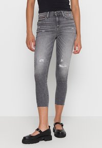Jeans skinny de tiro alto en gris con detalles desgastados, dobladillo deshilachado y diseño clásico de cinco bolsillos, combinados con zapatos gruesos negros.
