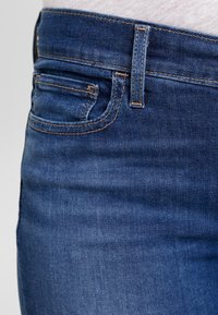 Mörkblå denimjeans med en figurnära design, synlig sömnad och en liten framficka. Slät textur med en lätt blekningseffekt.