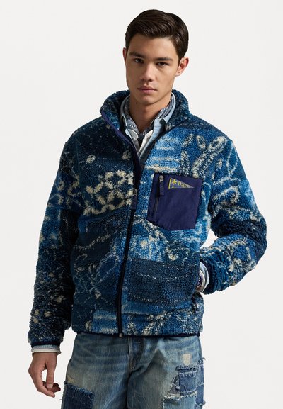 Blue fleece jacket featuring a textured pattern, high collar, zippered front, and a contrasting navy chest pocket with logo.