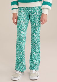 Pantaloni evazați cu model floral verde, confecționați dintr-un material moale, cu un design floral alb, asortați cu adidași gri și albi.