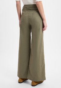 Olijf groene broek met wijde pijpen van lichtgewicht stof, met achterzakken en een hoge tailleband. Gecombineerd met bruine enkellaarsjes.