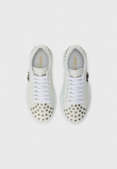 White sneakers with silver studded accents on the toe, featuring a textured upper, white laces, and gold branding on the insole.