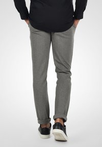 Grå skreddersydde bukser med en glatt tekstur, slim fit og rullede mansjetter. Kombinert med svarte joggesko med hvit såle.