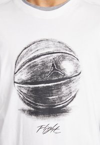 Camiseta blanca con un gran gráfico de baloncesto en negro y gris, con el logo de Jumpman y la palabra "Flight" en una fuente cursiva debajo.