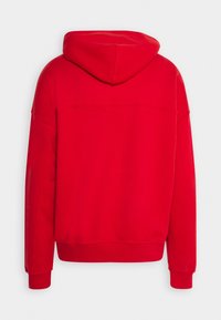 Czerwona bluza z dużym kapturem, ściągaczami przy rękawach i luźnym krojem. Wykonana z miękkiego materiału, w jednolitym kolorze bez dodatkowych wzorów.