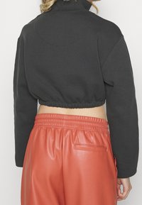 Klarad svart sweatshirt med hög krage, försedd med en hopkrupen nederkant. Matchad med högmidjade, glänsande rostfärgade byxor.