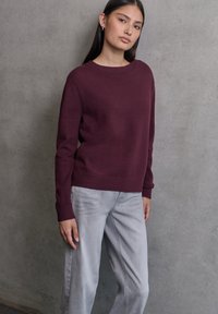 Pull en tricot bordeaux avec un col rond et des poignets côtelés, associé à un jean large gris clair. Tissu texturé sans motifs.