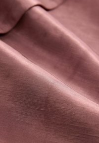 Materiał tekstylny w delikatnym, różowym odcieniu z gładką teksturą, z subtelnym połyskiem i drobnym, tkanym wzorem.
