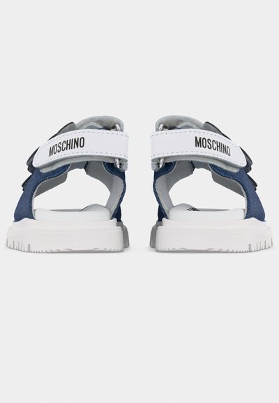 Οπίσθια όψη μπλε και λευκών σανδαλιών Moschino με ρυθμιζόμενες λευκές λωρίδες που φέρουν μαύρο λογότυπο της μάρκας και χοντρές λευκές σόλες.