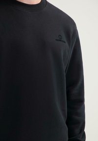 Czarna bluza wykonana z mieszanki bawełny, z okrągłym dekoltem, ściągaczami na rękawach i małym logo na piersi. Gładka tekstura, standardowy krój.