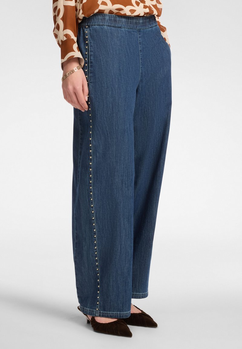 Szerokie dżinsowe spodnie w ciemnoniebieskim kolorze z złotymi ćwiekami wzdłuż bocznego szwu. Charakteryzują się luźnym krojem i elastycznym pasem dla wygody.