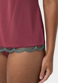 Top bordeaux ornée d'une délicate bordure en dentelle teal avec un ourlet festonné, conçu avec une texture lisse et une coupe décontractée.