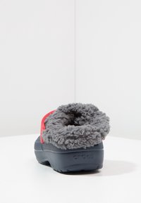 Szara kapcie z meszkiem, granatową podstawą i czerwonym paskiem akcentującym. Podeszwa o fakturze zapewniającej przyczepność oraz zaokrąglone zapięcie z tyłu.